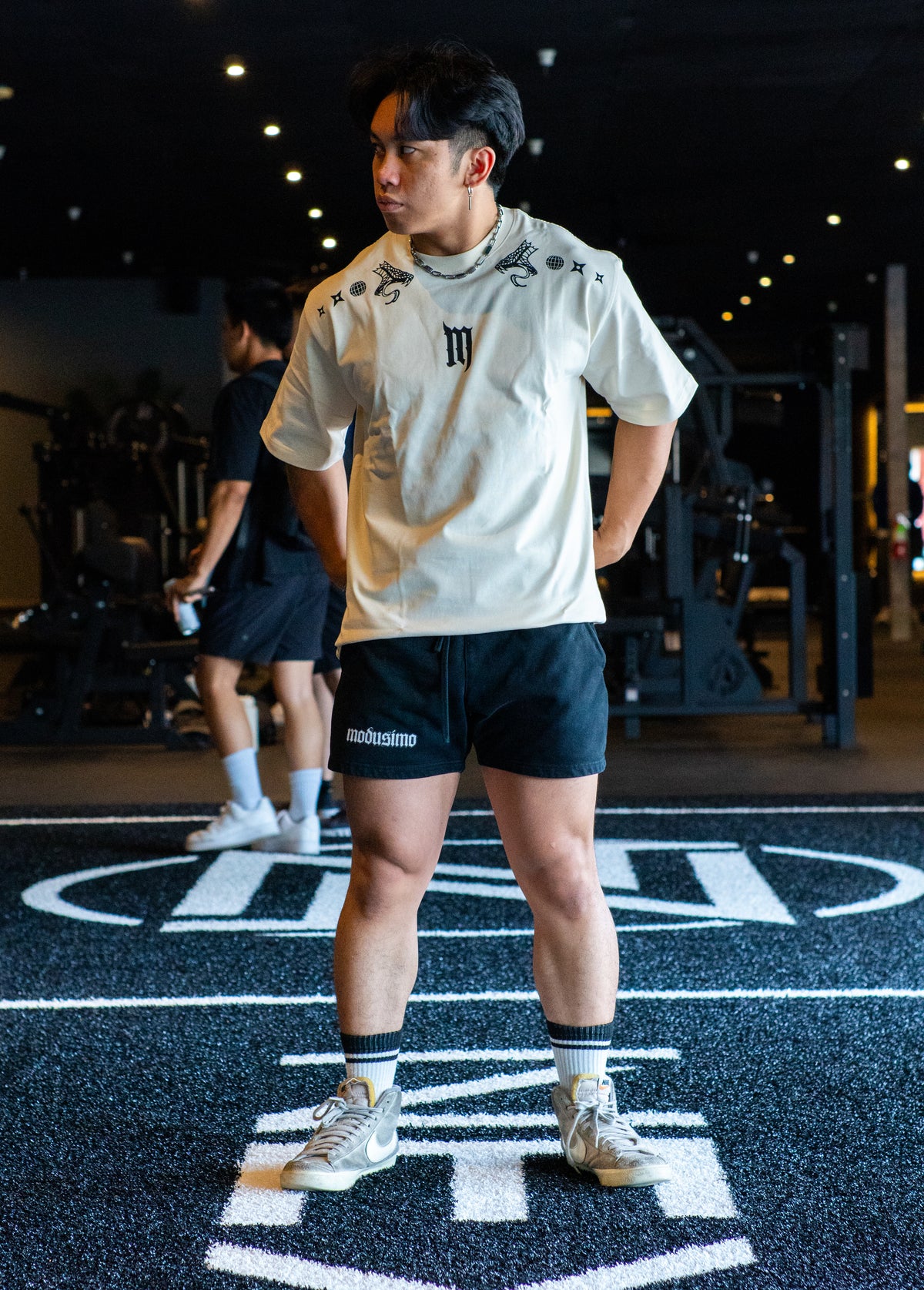Model wearing the Kenshin Premium oversized tee in pastel cream with black shorts, in the gym — second view