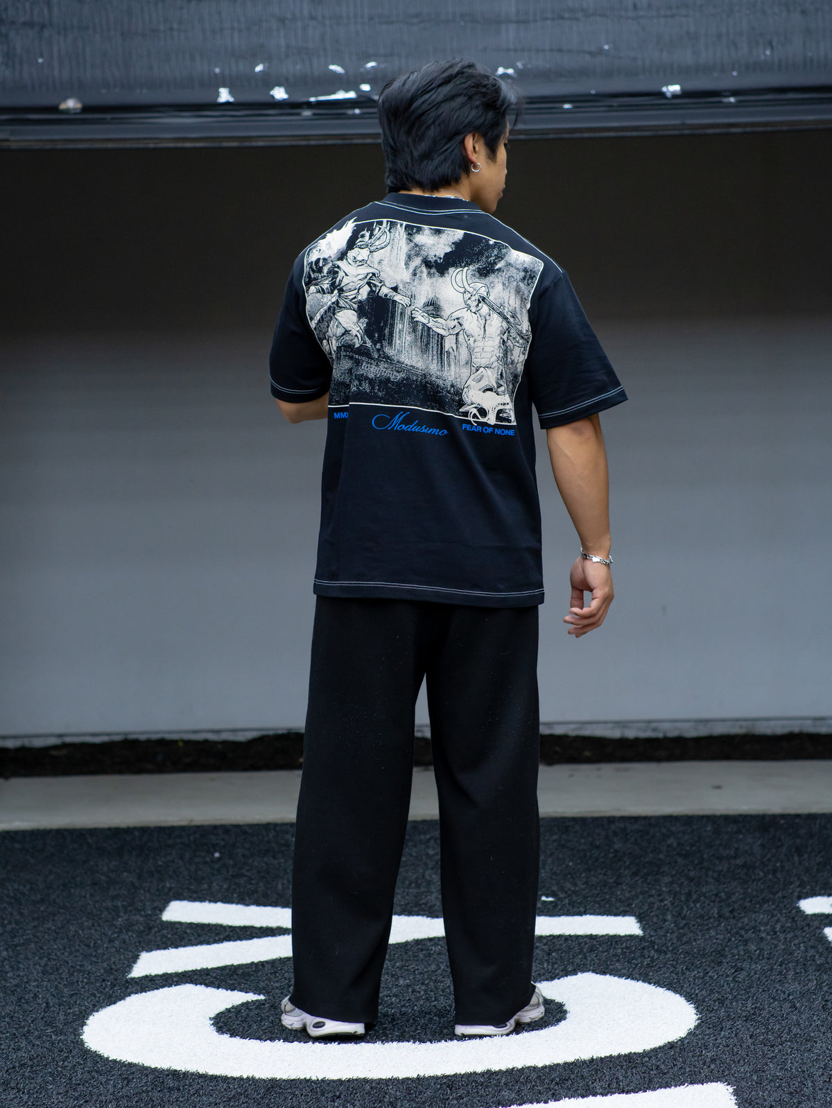 Model from behind wearing the Gatekeeper Premium oversized tee in black, in the gym — second view