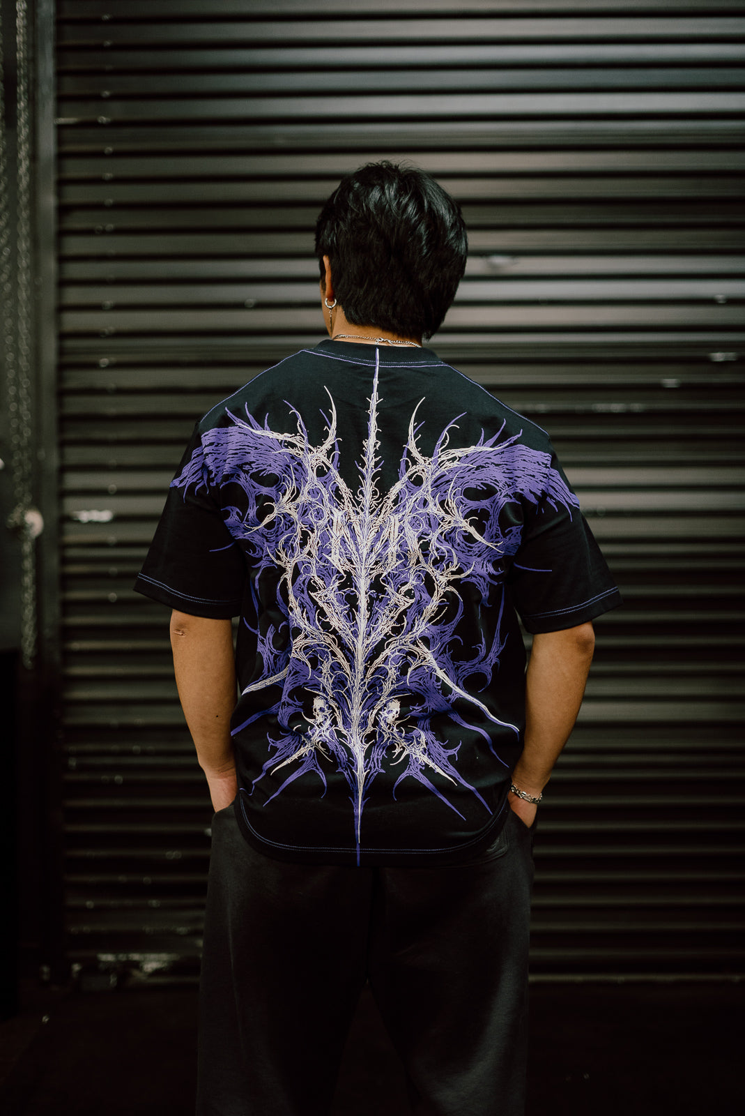 Model from behind wearing the Nightcrawler Premium oversized tee in black with purple wing print — second view