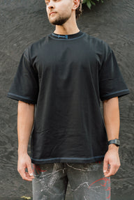 Model wearing the Motivated Premium oversized tee in black, front view with blue contrast stitching