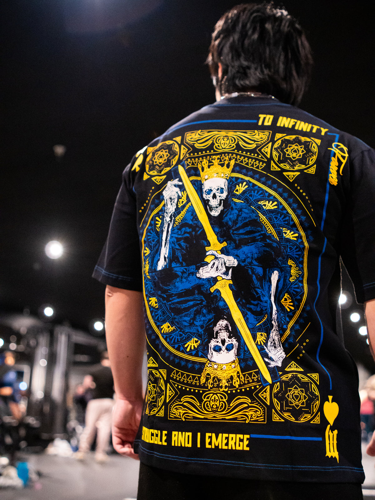 Close-up of the Royal Flush blue and gold card back print on the black Premium tee, worn — second view