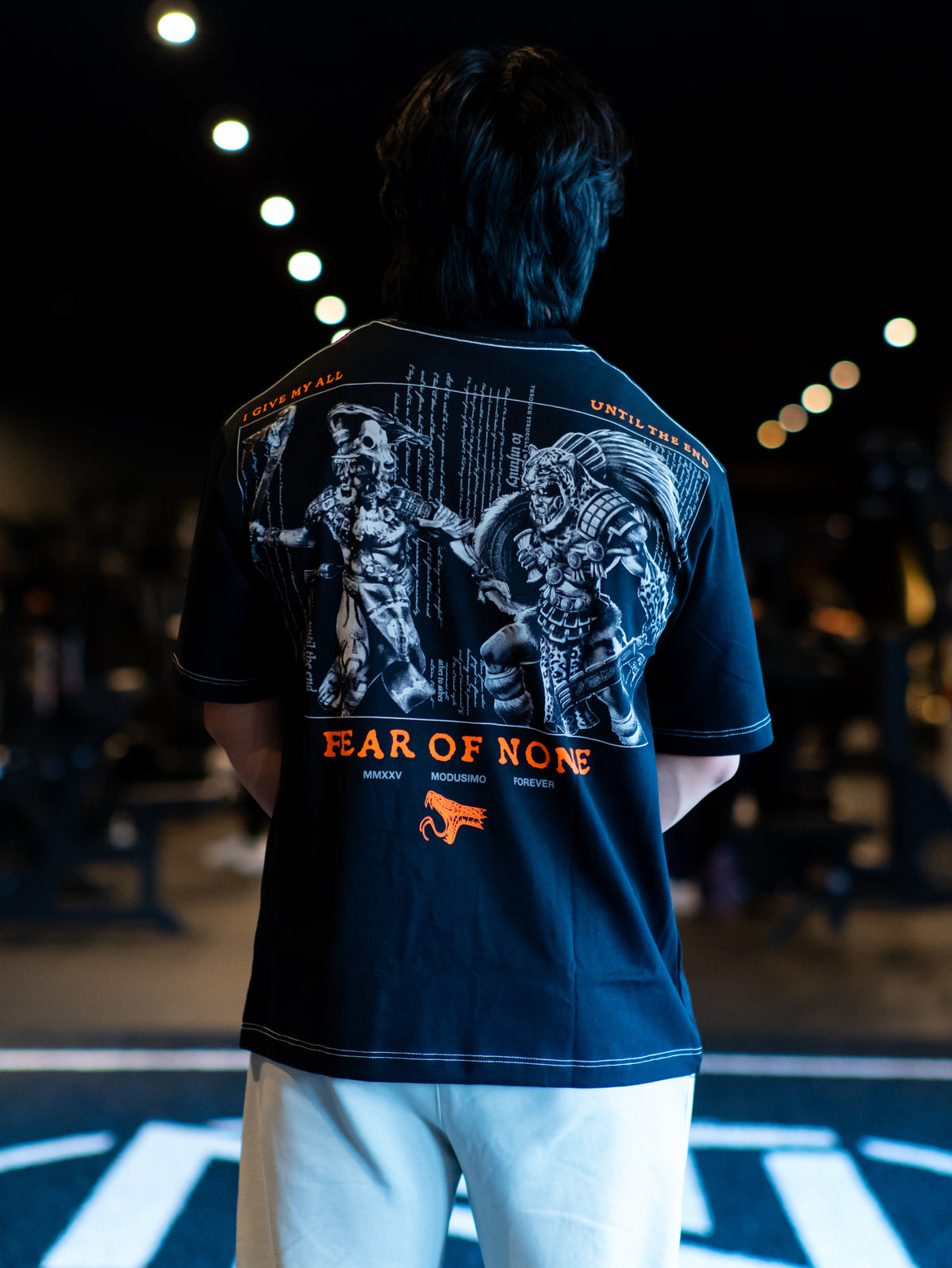 Model from behind wearing the Fear of None Premium oversized tee in black, in the gym — second view