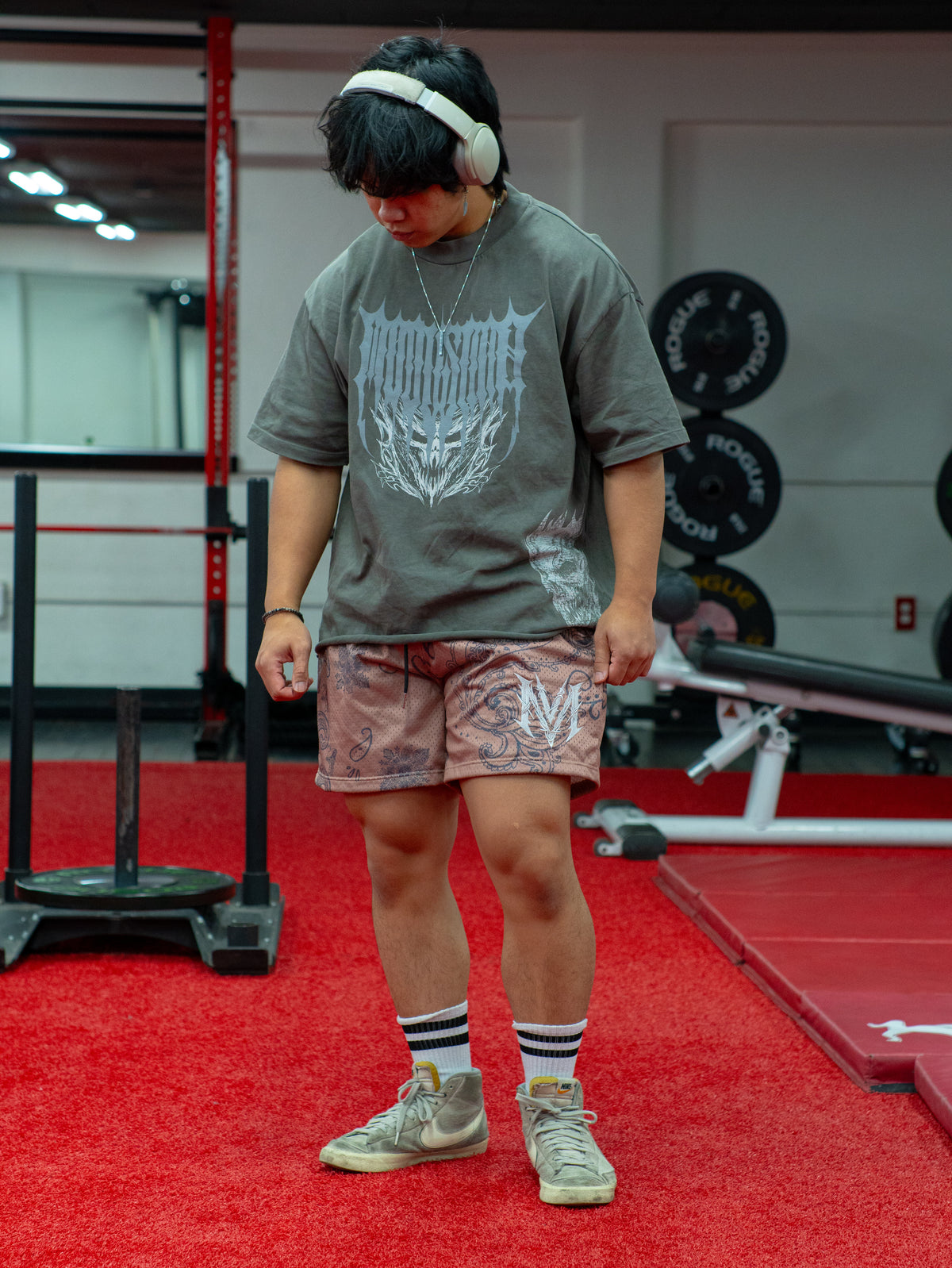 Model wearing the Carry the Torch mesh shorts in sandstorm with a gray tee, in the gym — second view