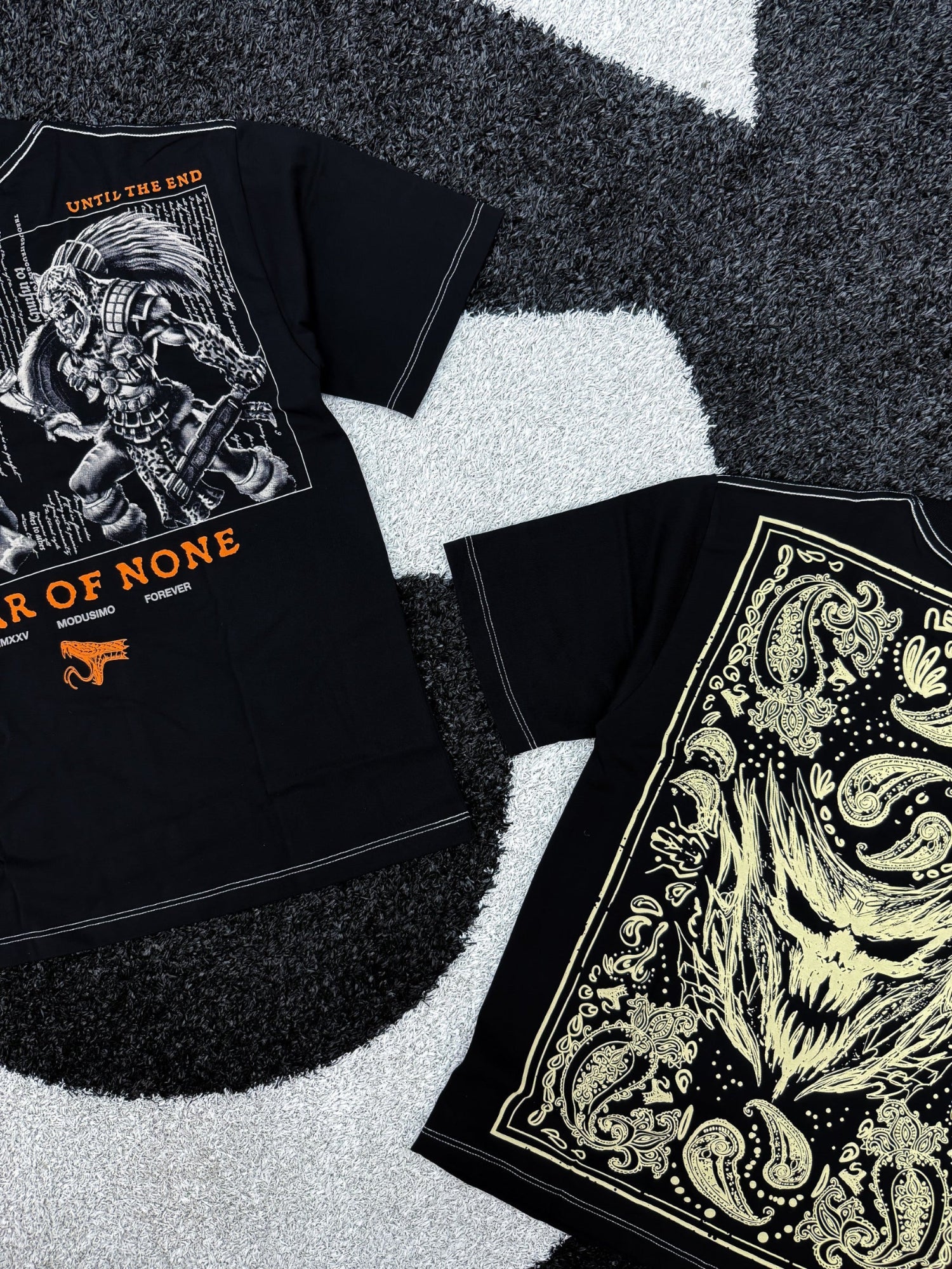 Two black t-shirts with graphic designs on a textured surface